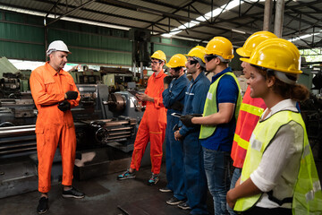 Supervisor giving a safety briefing to factory workers in helmets